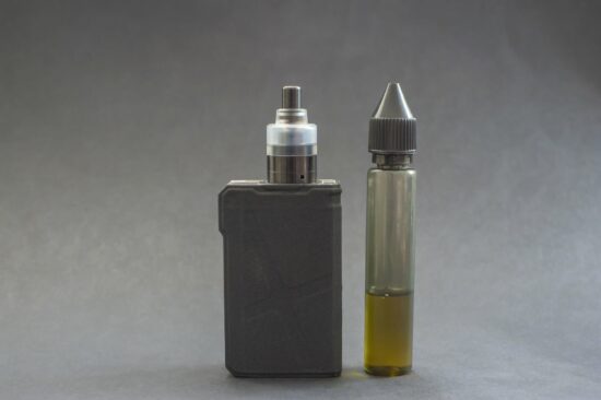 e-zigarette.jpg Ein Verdampfergerät links, daneben eine Flasche mit E-Liquid in einer transparenten Verpackung.